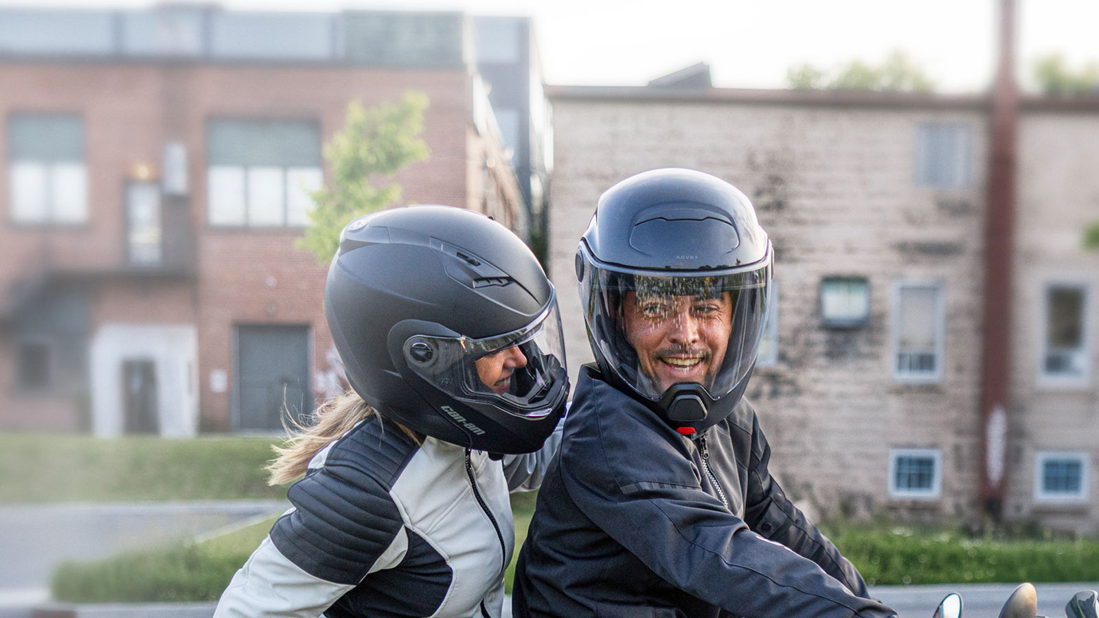 Two smiling riders sporting the new Can-Am Exome Modular Helmet while riding