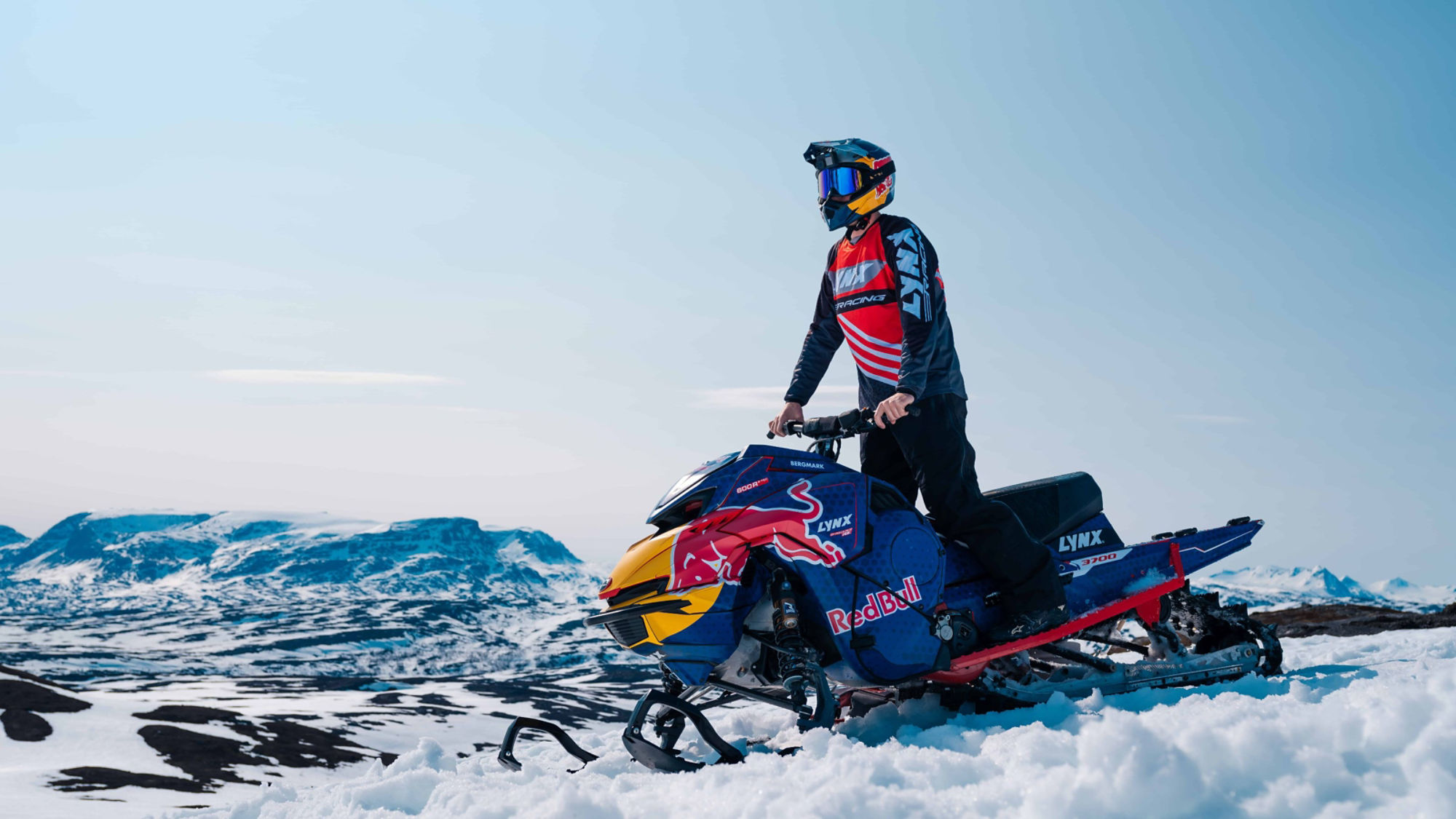 Rider performing a trick on a 2026 Lynx Shredder RE snowmobile in a snowy forest.