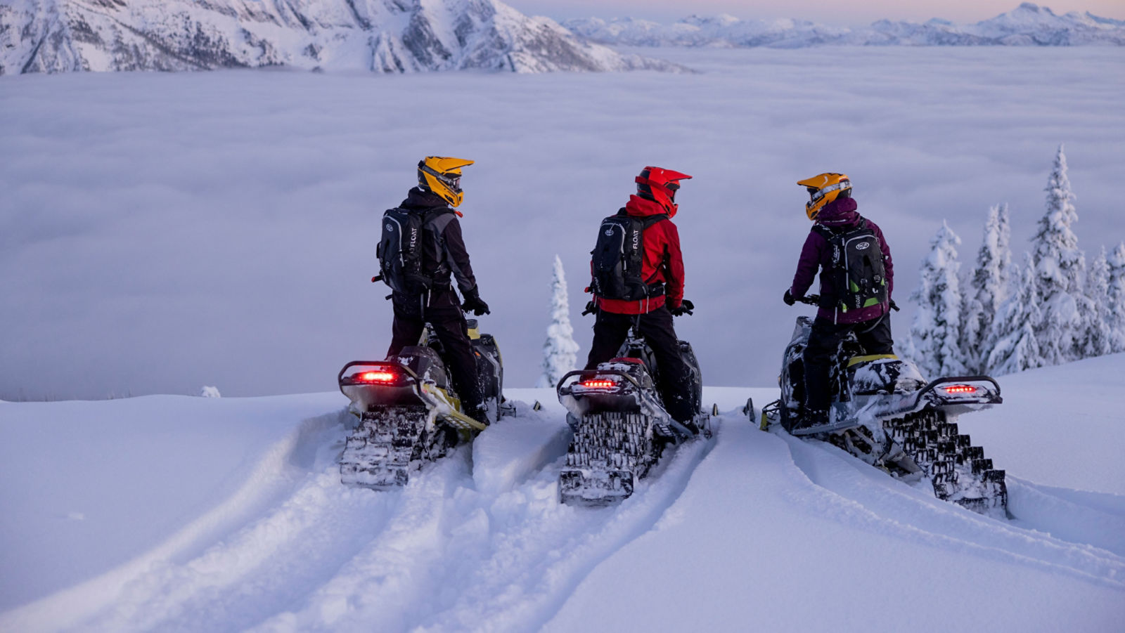 Tre snøscooterførere som tar en pause på fjelltoppen