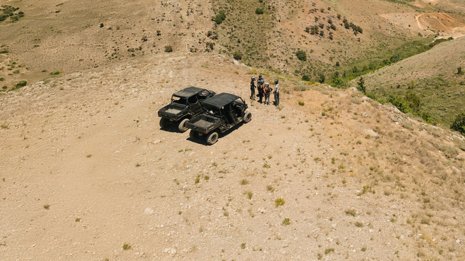 Four people standing atop a mountain with two Can-Am Side-by-side (SxS) vehicle