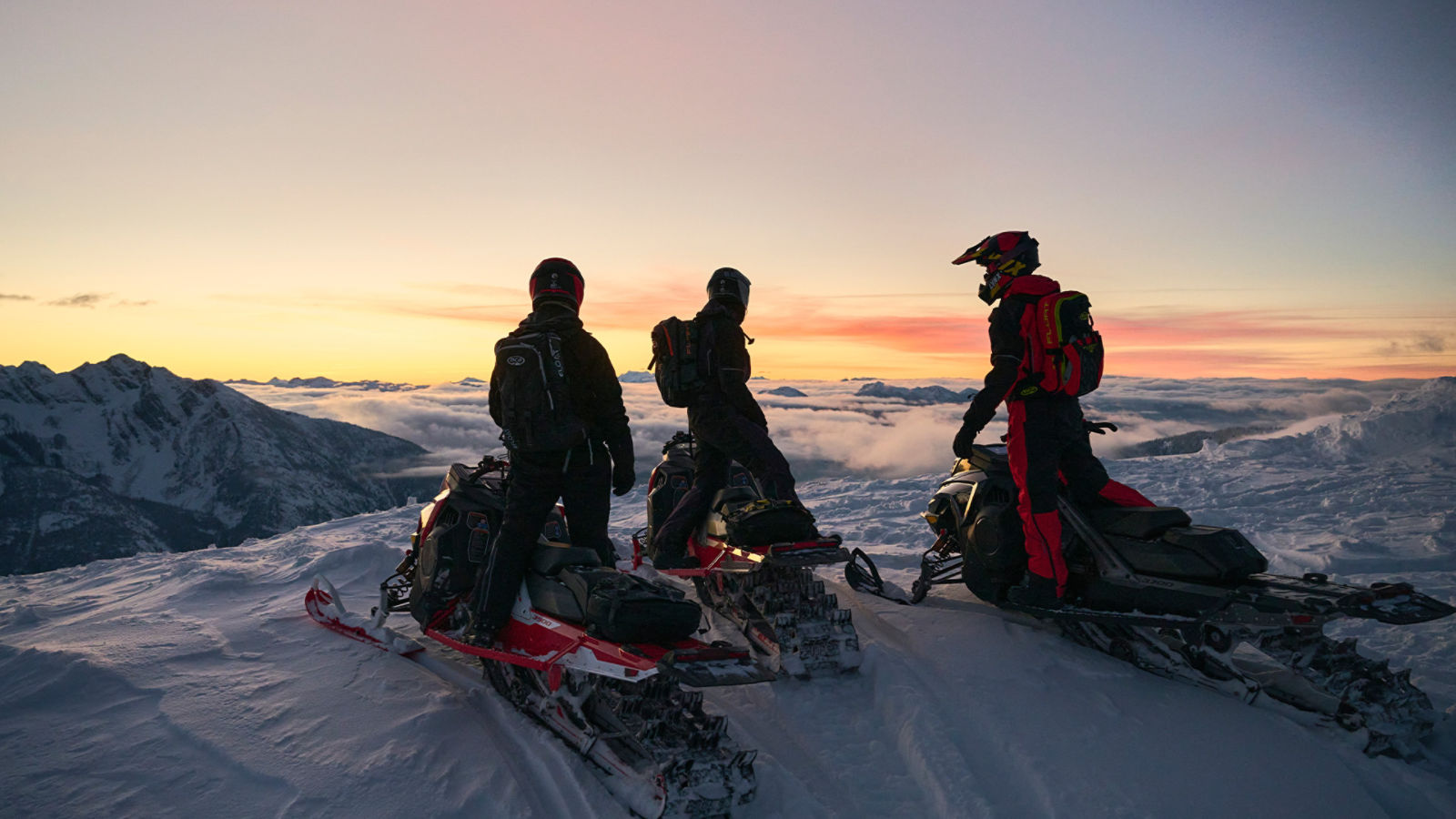 Tres motonieves de pie en la cima de una montaña