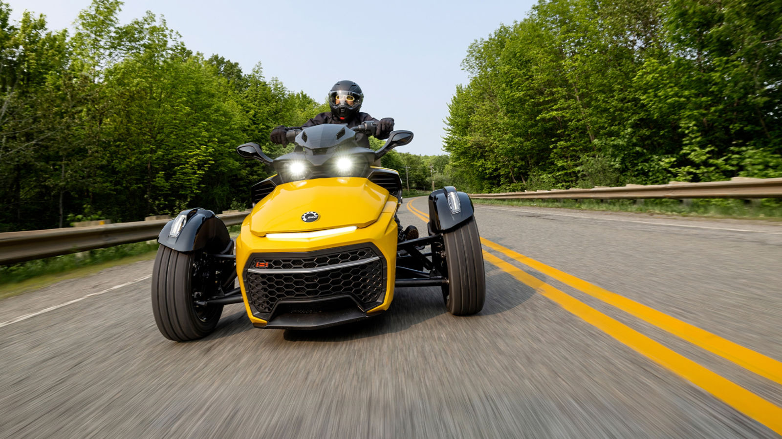 Conductor circulando en un vehículo de tres ruedas amarillo por una carretera.