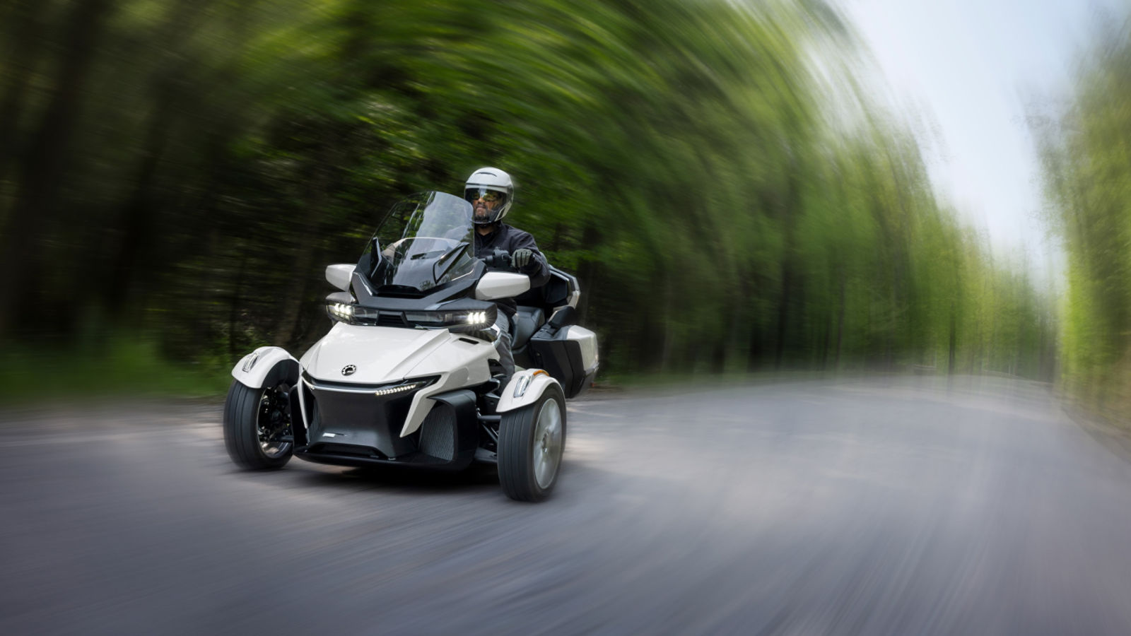 Man riding a Can-Am Spyder RT 3-wheel vehicle on a road surrounded by trees