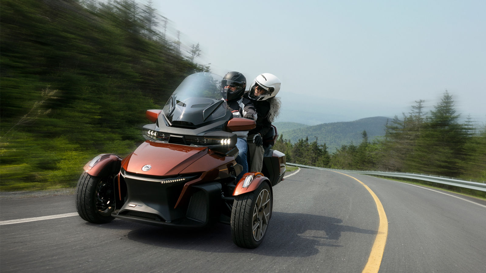 A couple riding a touring 3-wheel from Can-Am on a paved road in the mountains