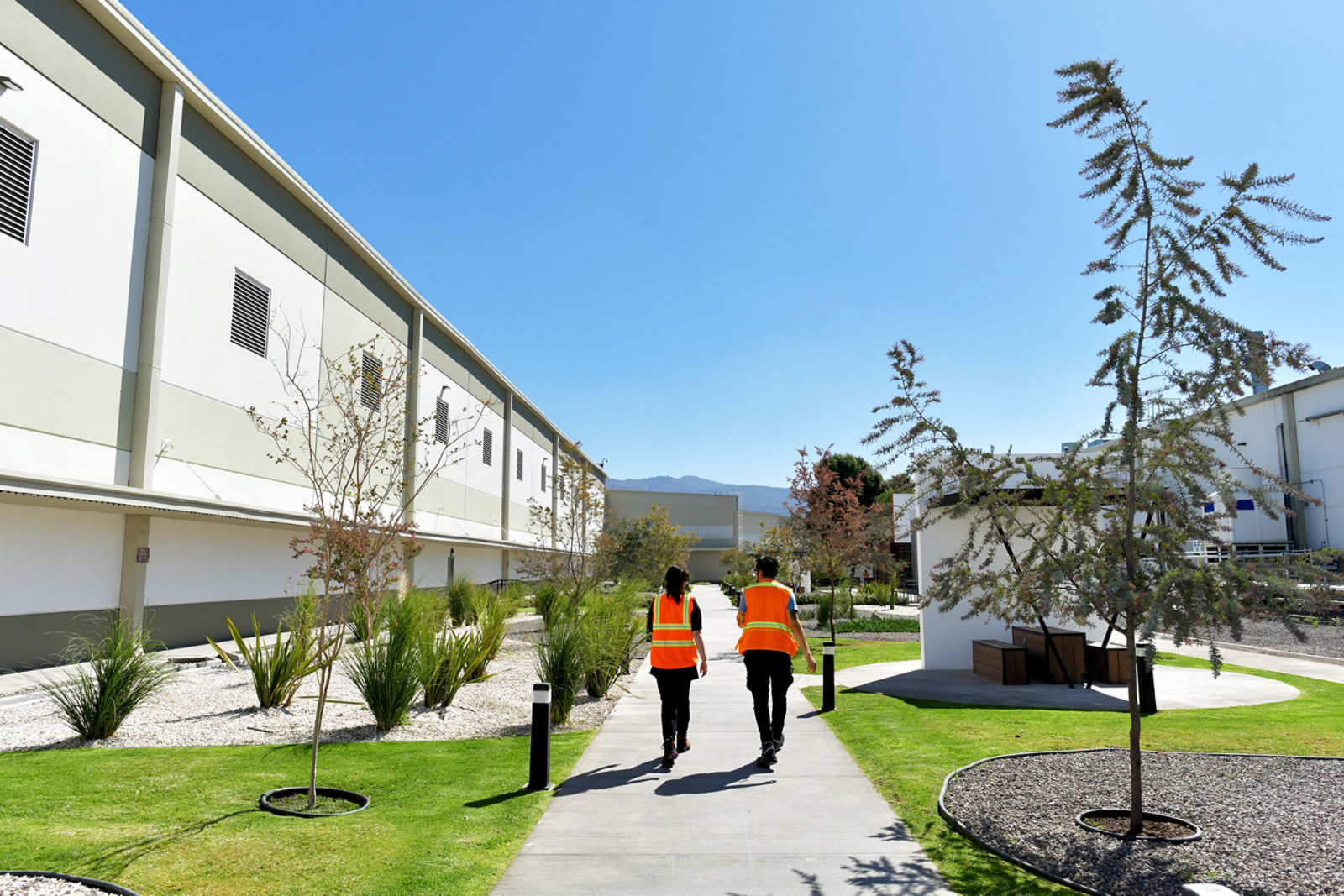Dos personas con chaleco de seguridad caminando junto a un edificio.