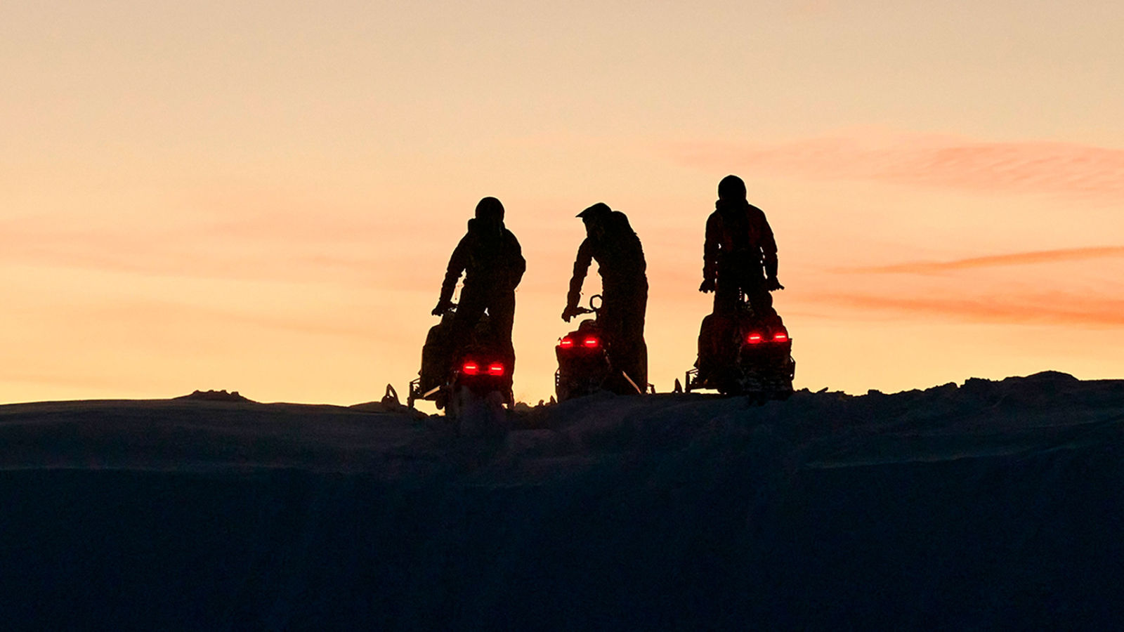 Kolme Lynx-moottorikelkkaa auringonlaskussa kukkulan päällä