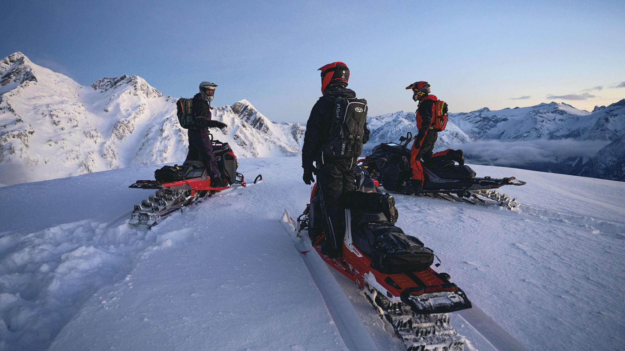 Three Lynx riders on their snowmobile at the top of a mountain