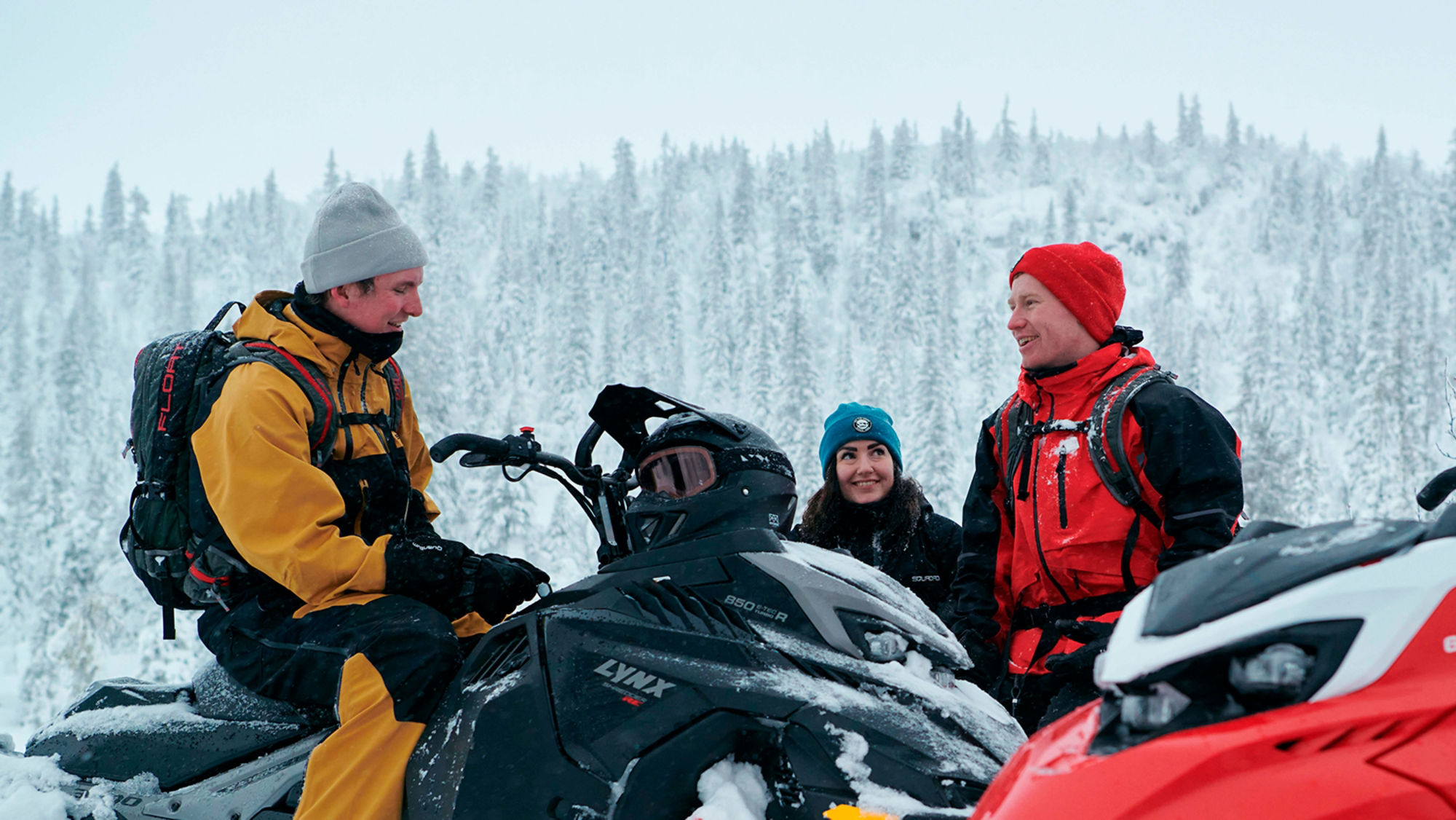 Three guys chatting and laughing on Lynx Shredder snowmobiles