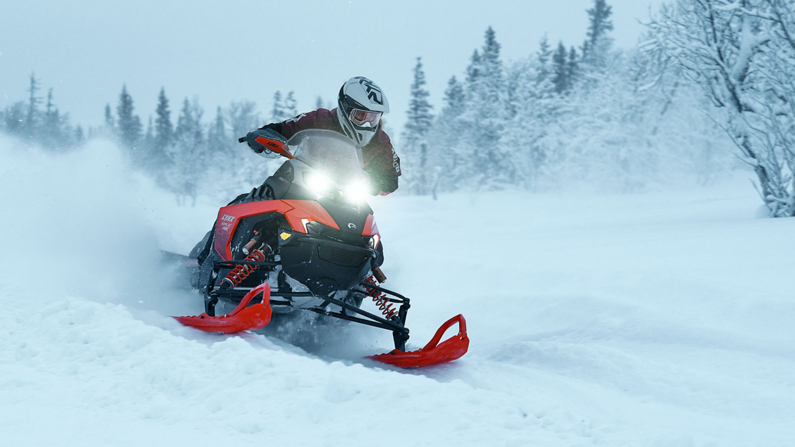 Snowmobiler riding the 2026 Lynx Rave RE snowmobile through deep snow in a forest.