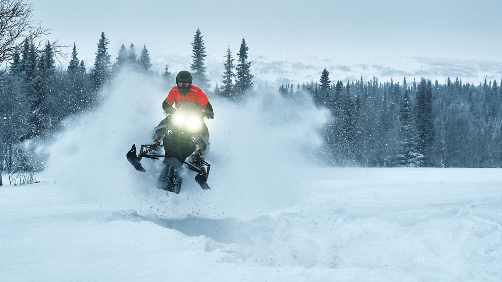 Snowmobiler making a jump on his 2026 Lynx Rave RE 2026 snowmobile in a snowy forest.