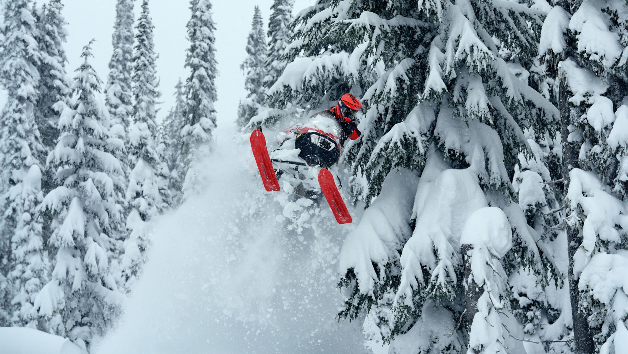 Motoneigiste sautant dans les airs avec sa motoneige Lynx Shredder RE 2026 dans une forêt enneigée.