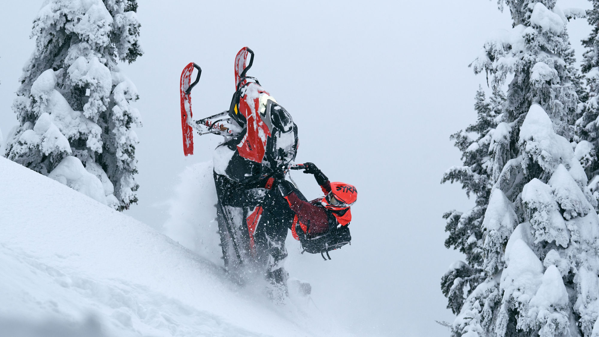 Rider performing a trick on a 2026 Lynx Shredder RE snowmobile in a snowy forest.