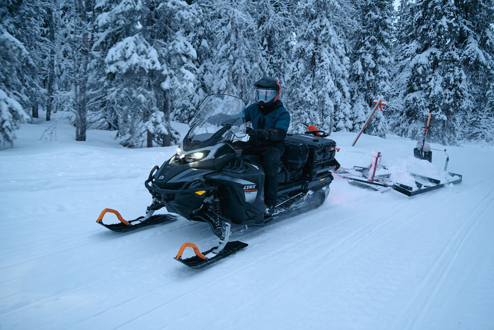 2027 Lynx 69 Ranger riding through a snowy forest pulling a sled