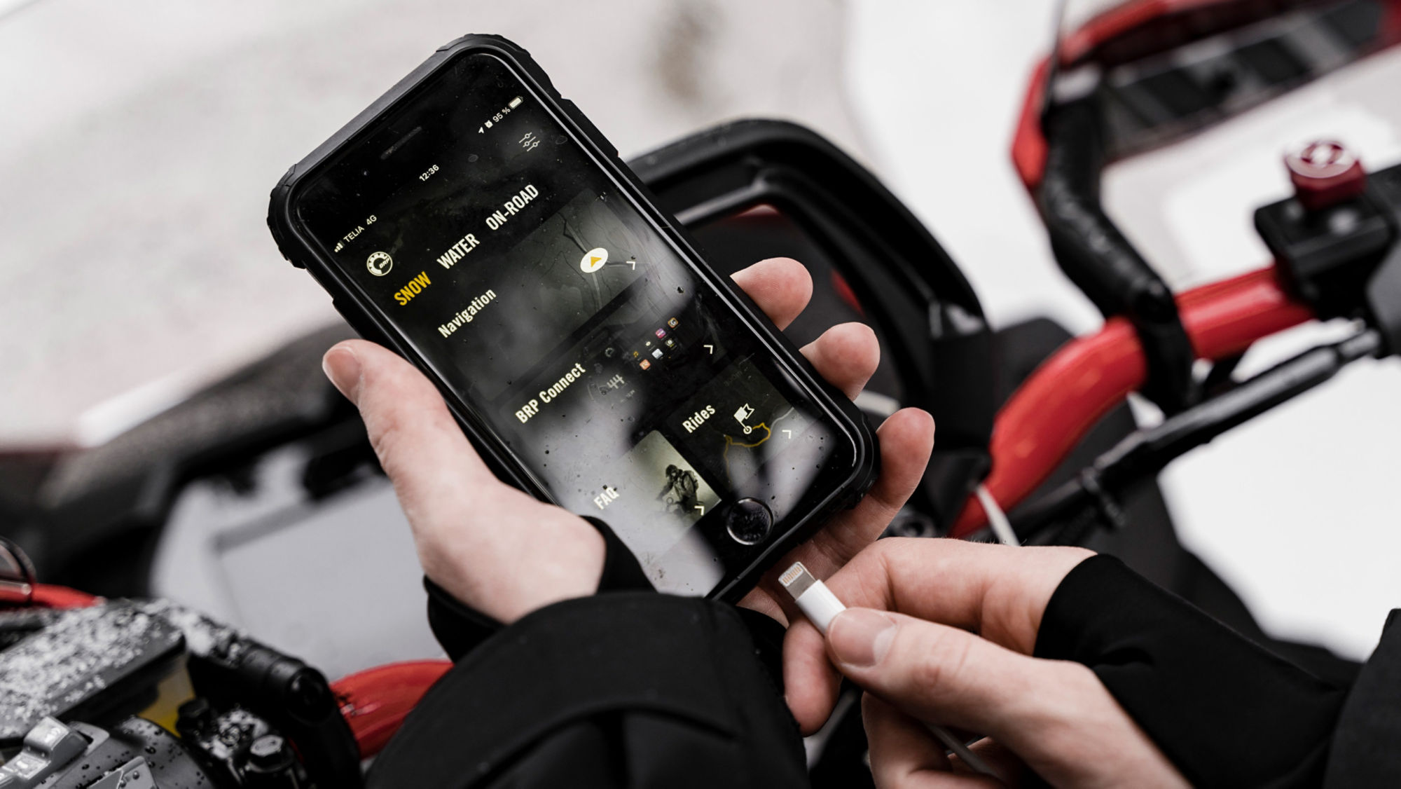 Rider attaching a charging cable to a mobile phone with BRP GO! App interface