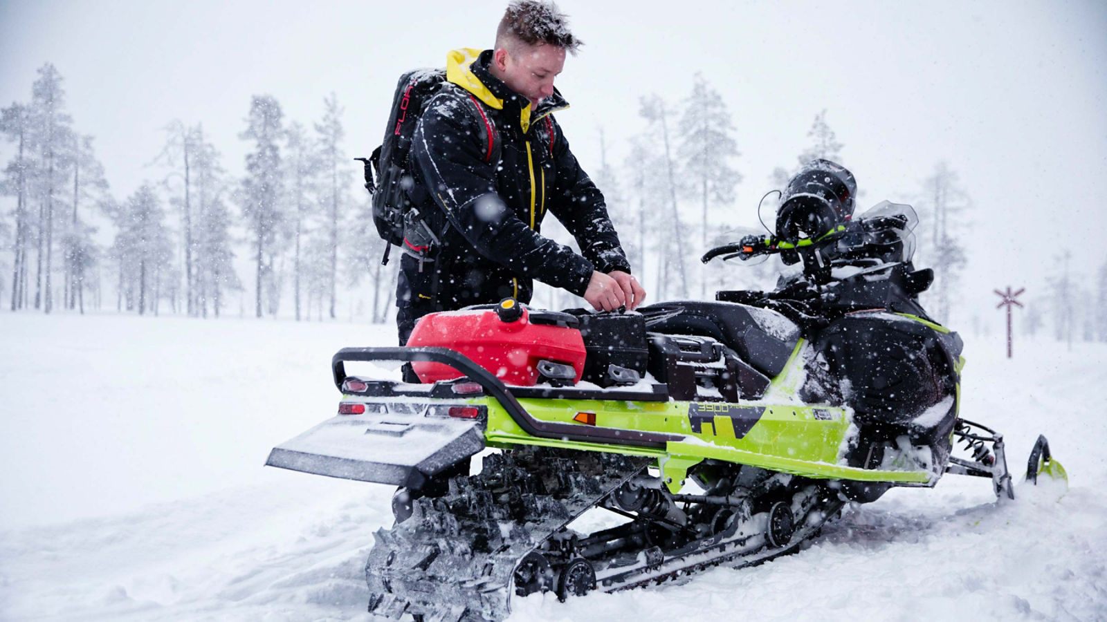 A man fixing his carrying items on his Lynx snowmobile's tunnel with the integrated LinQ accessory system.