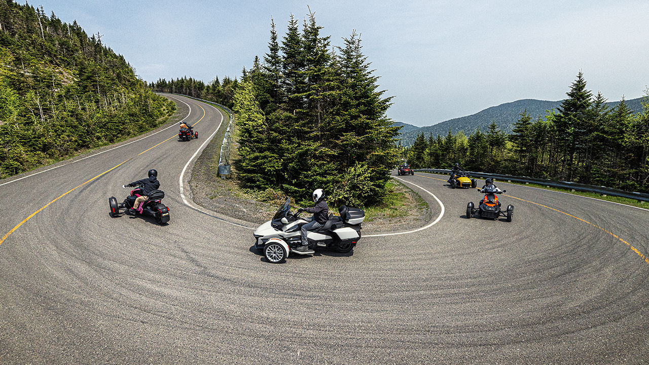 Several different models of Can-Am three-wheelers driving one behind the other on a winding road