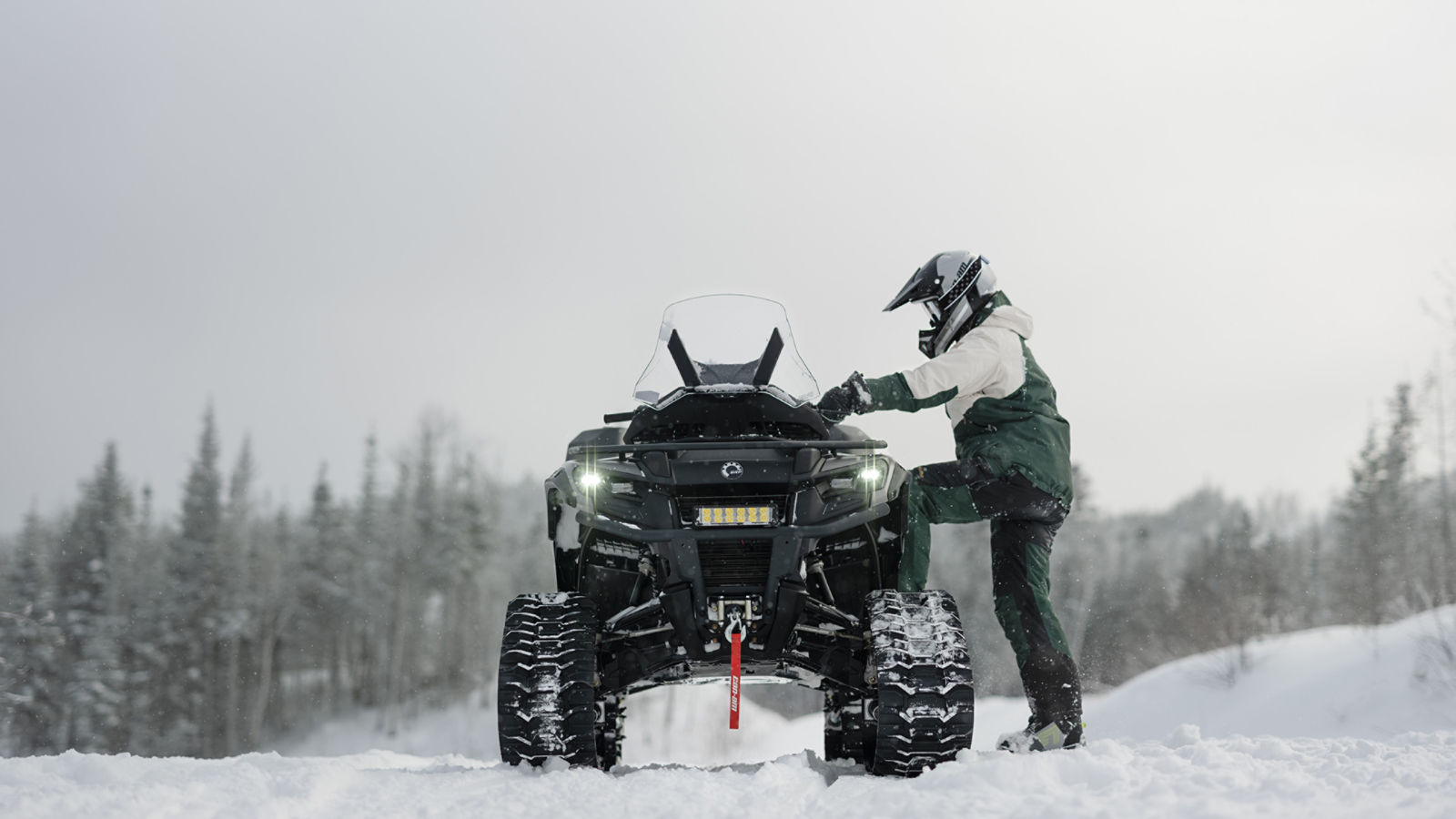 Un homme sur le point de monter sur un Can-Am Outlander, équipé d'un système de chenilles, sur un sentier enneigé