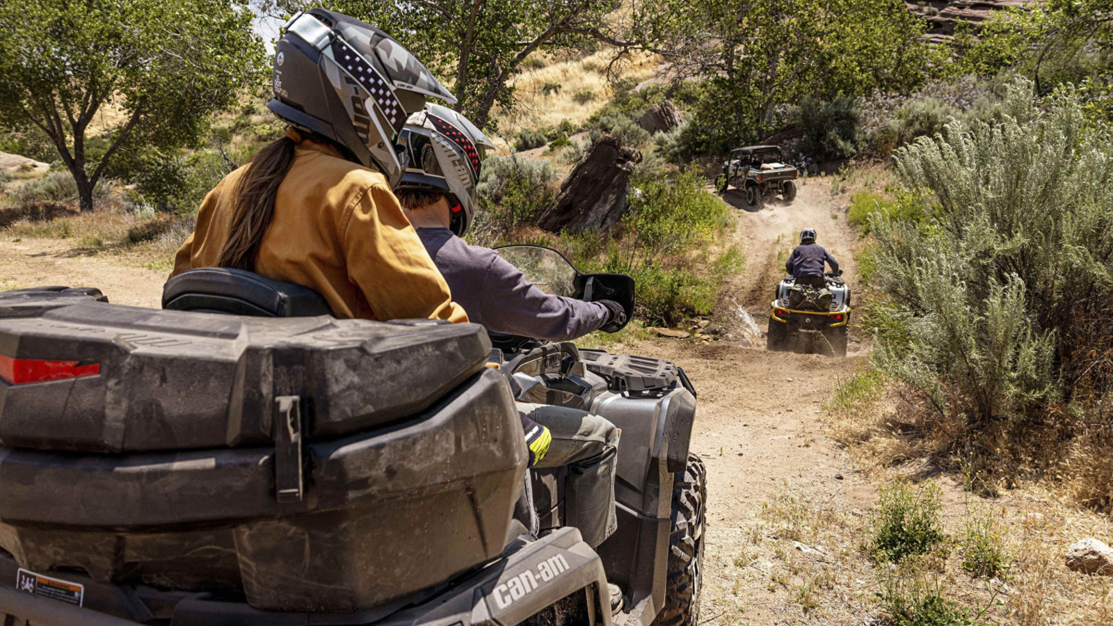 Two Can-Am ATV and a side-by-side vehicle following each other on a desert trail
