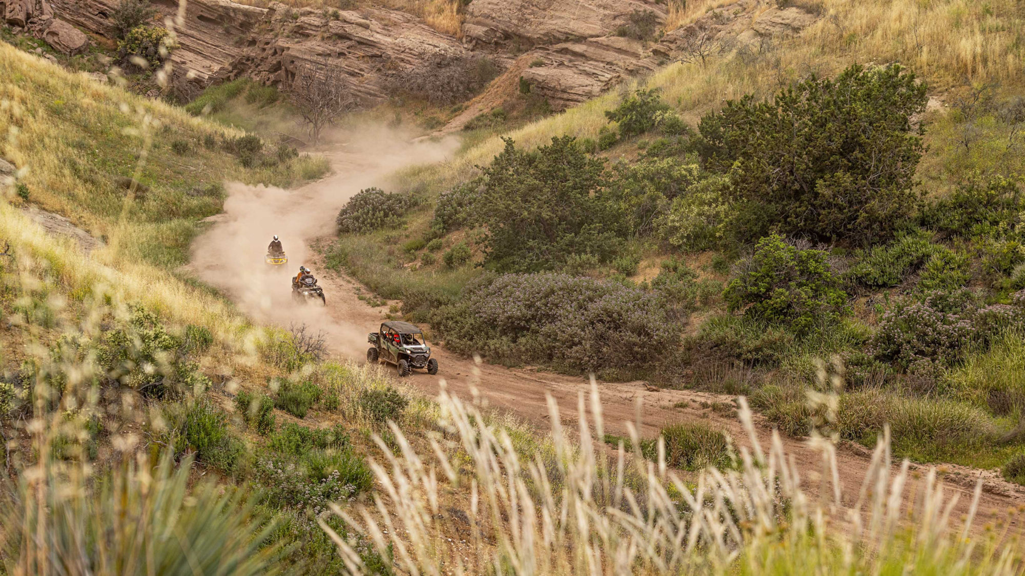 Two ATVs and one side-by-side, riding on an unpaved road 