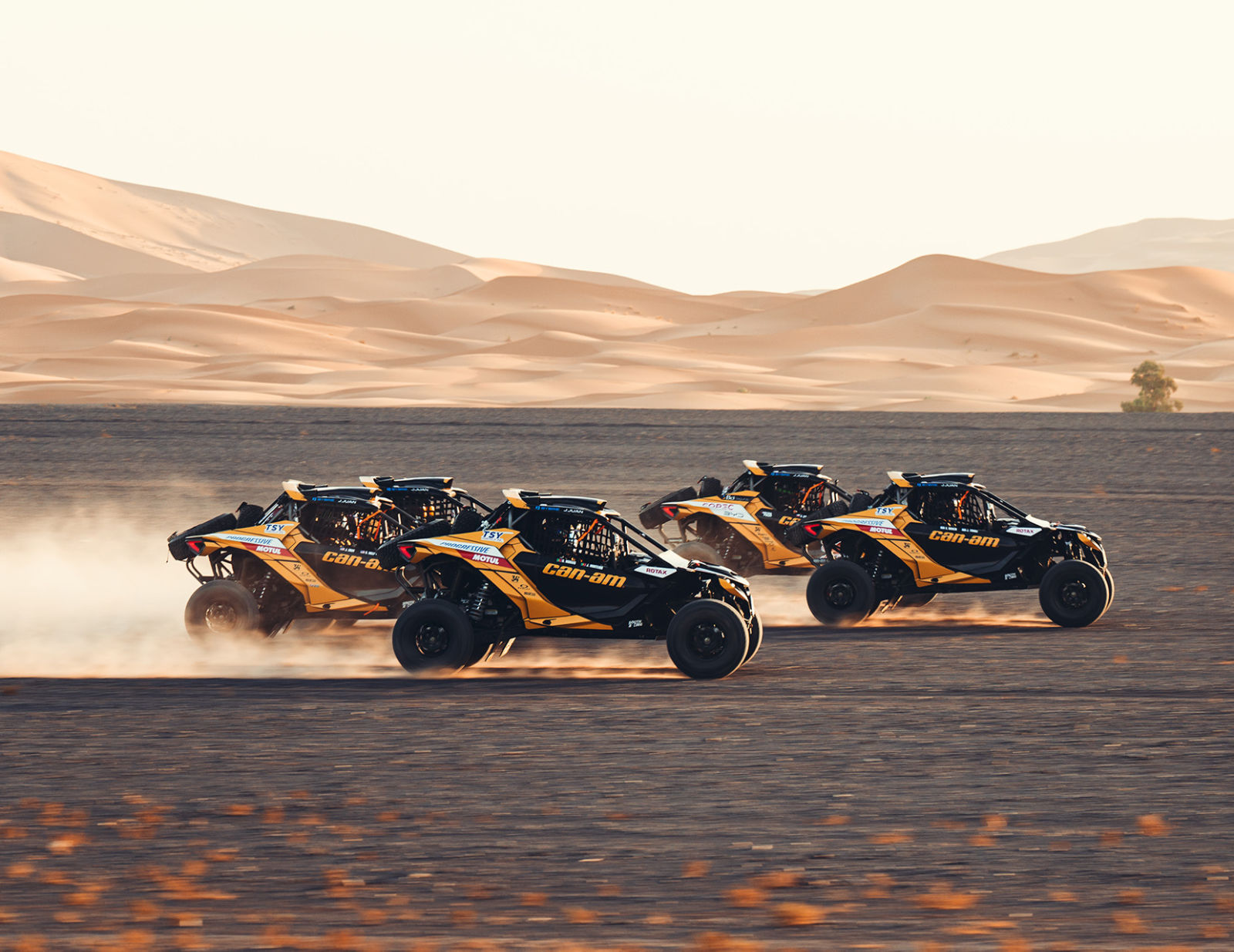 A Can-Am Maverick R X RS 2025 rolling down a sand dune on a sunny day