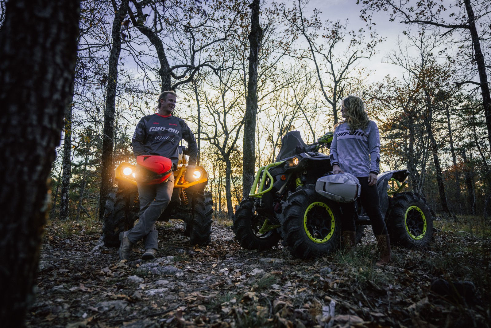 Two ATV riders dressed in Can-Am apparel with the sun setting behind