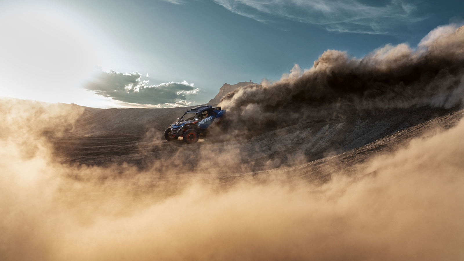 Un Can-Am Maverick X RS en drift dans les dunes de sable, laissant un nuage de poussière derrière