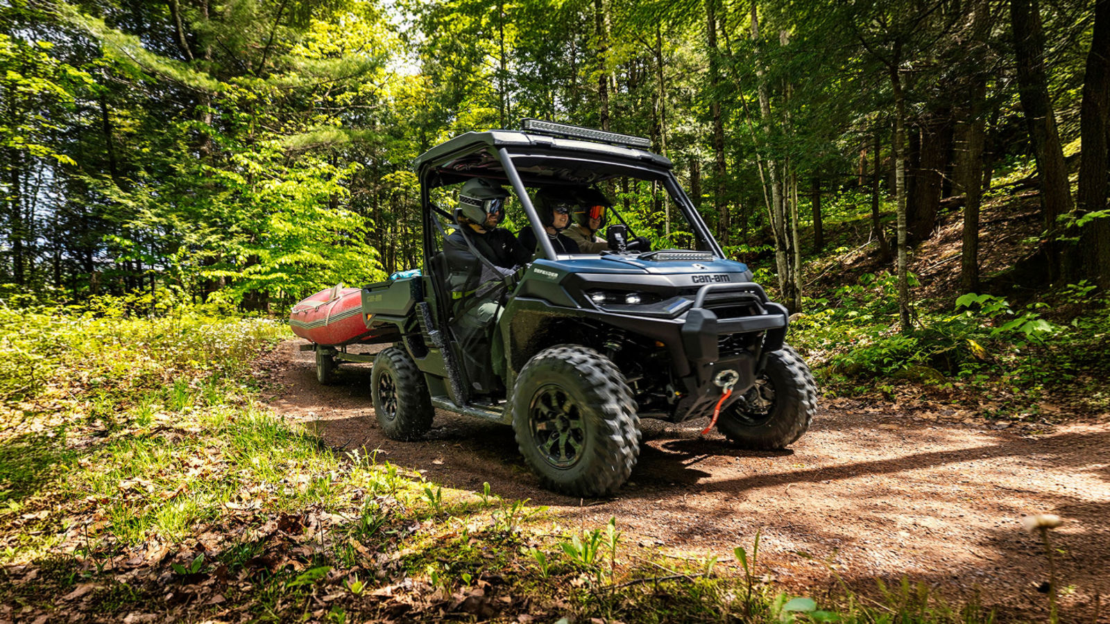 Three drivers on a Can-Am Defender side-by-side vehicle pulling a boat through the forest