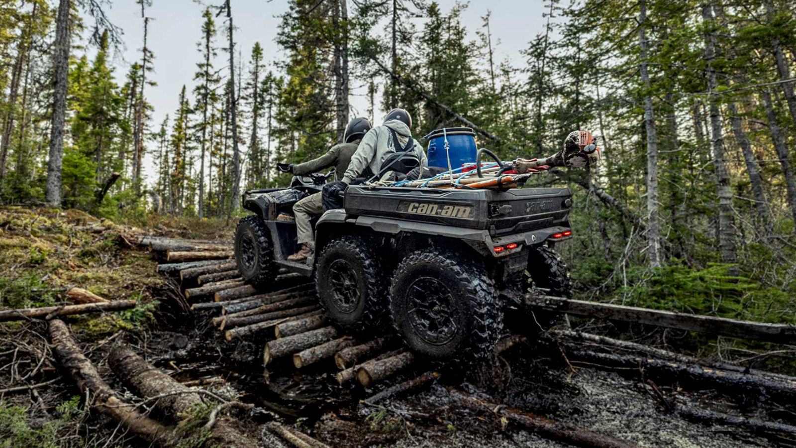 Two men on a 6-wheel Can-Am ATV riding over tree trunks and carrying several tools 