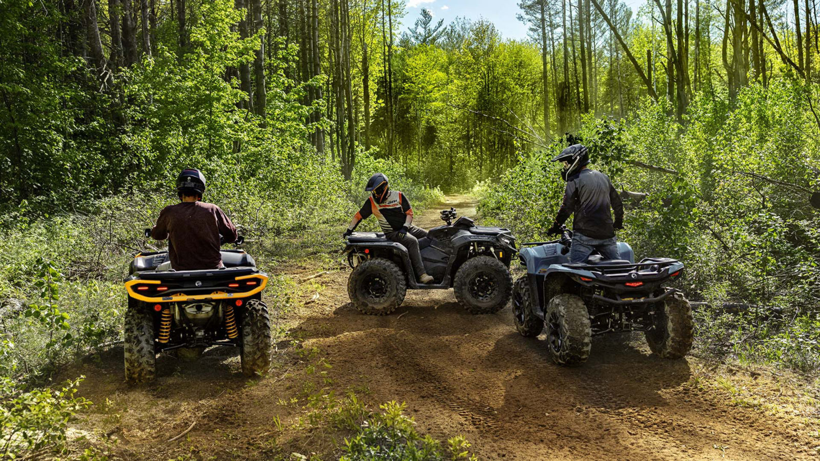 Several 2026 Can-Am Outlander ATV models on a forest dirt road