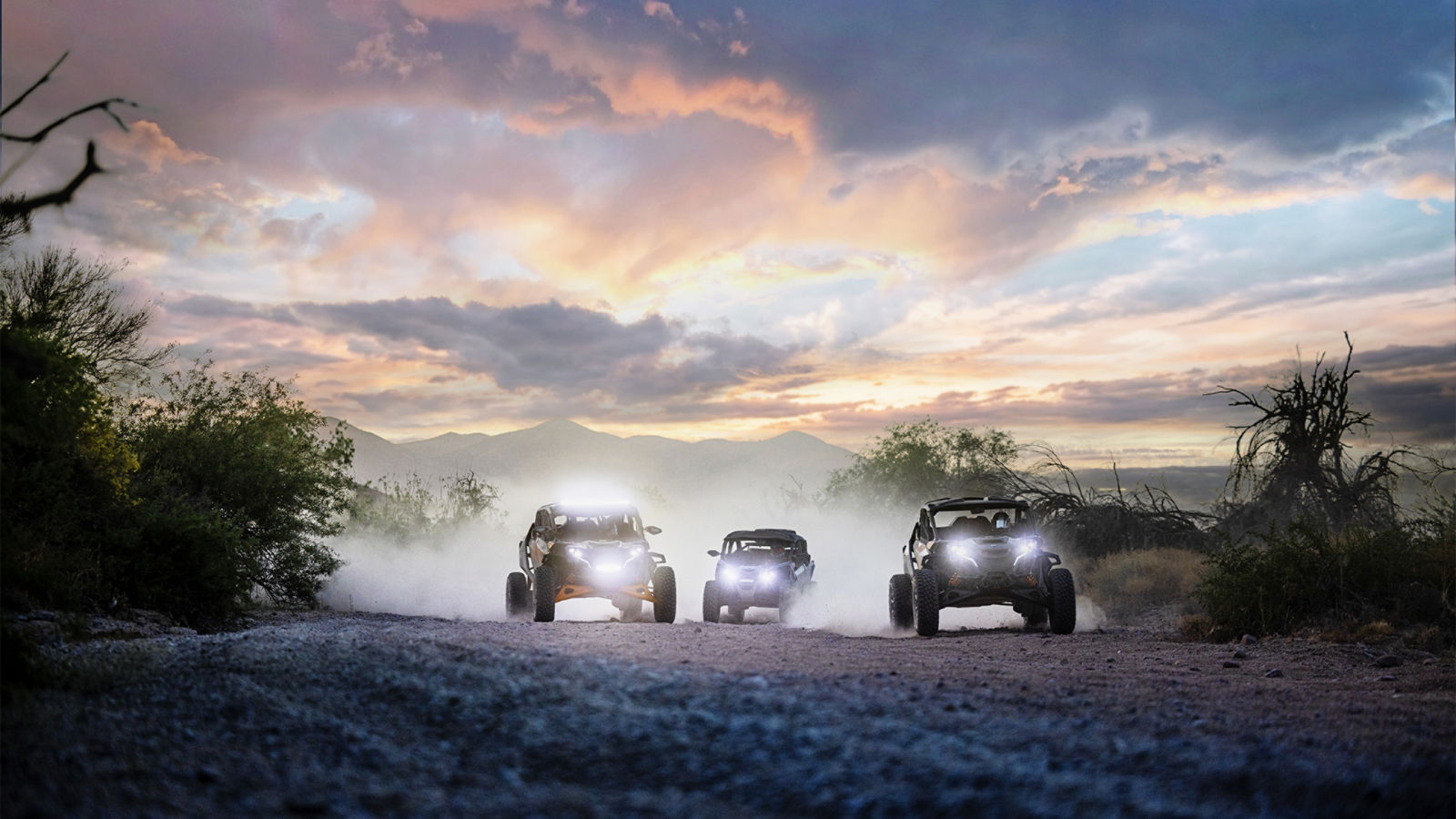 Three Can-Am side-by-side vehicles in the desert at dusk, showcasing their headlights