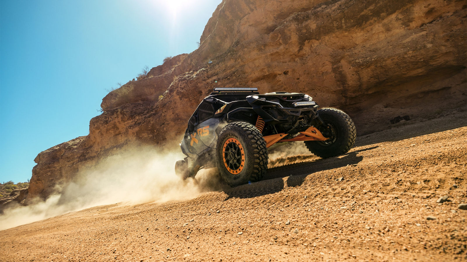 2027 Can-Am Maverick MAX X-RS rijdend in het zand naast een rotswand