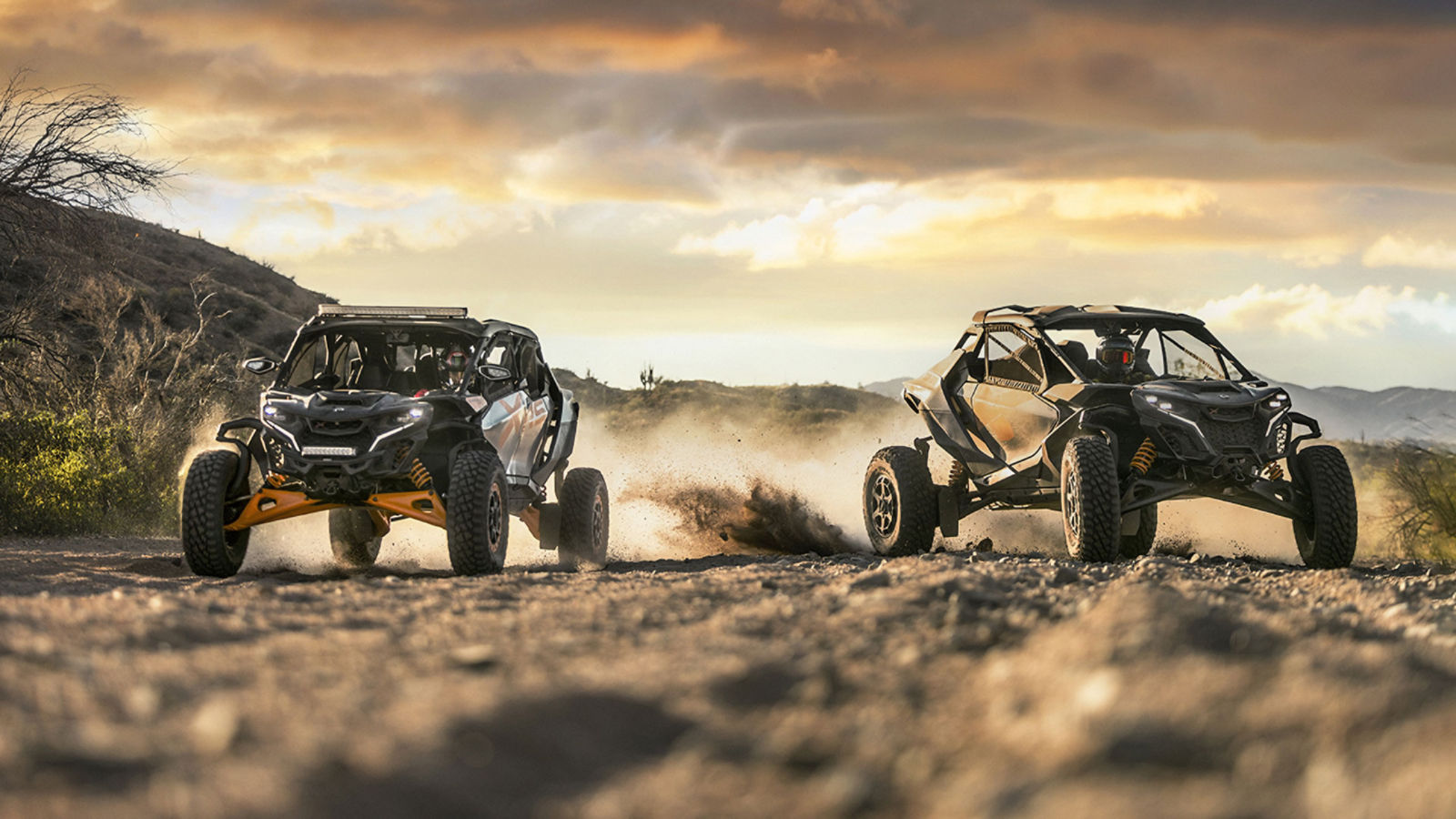 Two Can-Am Maverick side-by-side vehicles riding in the desert at sunset