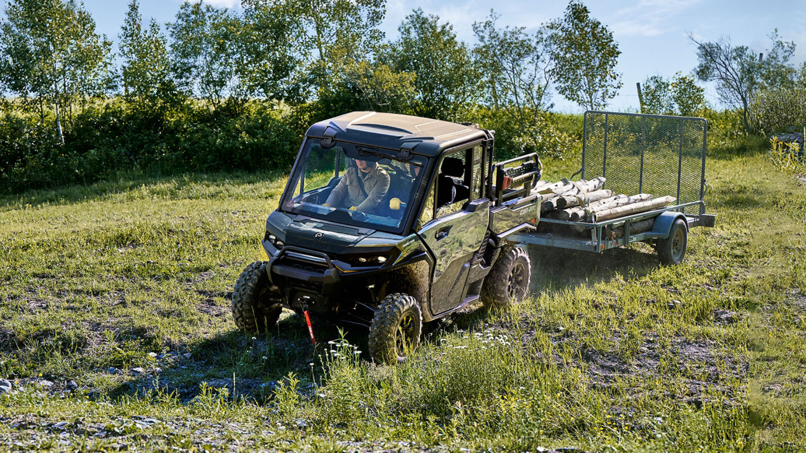 Dos conductores en un vehículo side-by-side Can-Am Defender XU XT CAB 2027 remolcando un remolque cargado con troncos