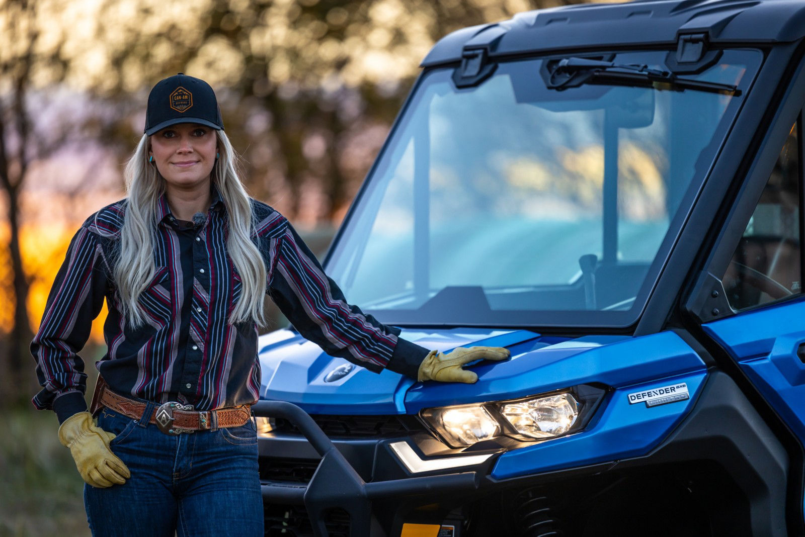 Close up of Alex Templeton leaning on the hood of her Defender in front of a setting sun. 