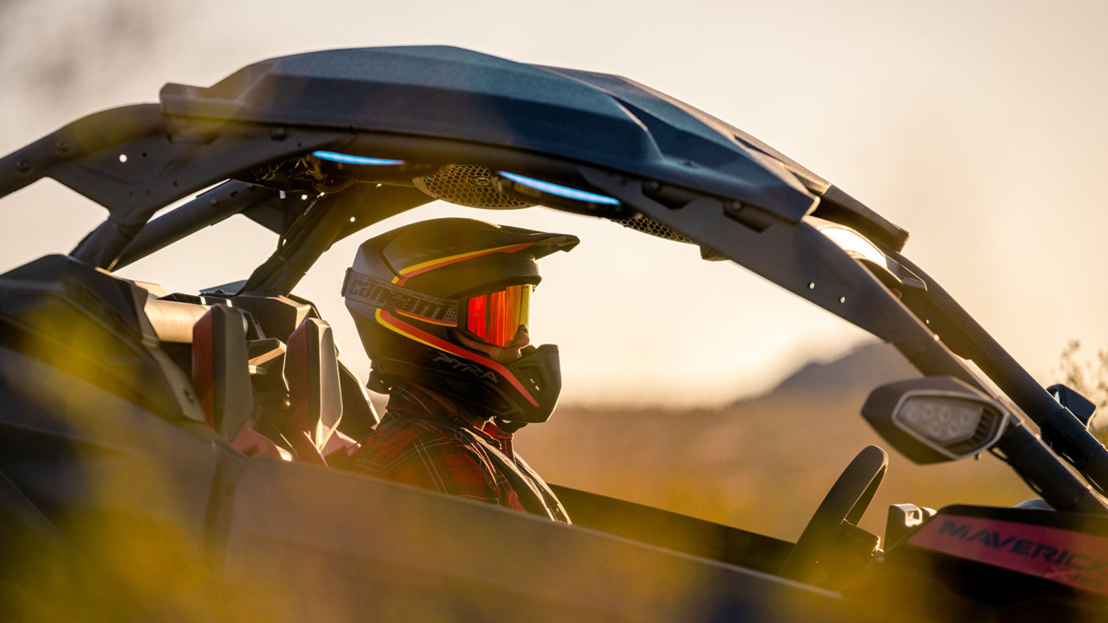Side profile of a rider wearing a branded Can-Am off-road helmet & goggles sitting in a side-by-side vehicle