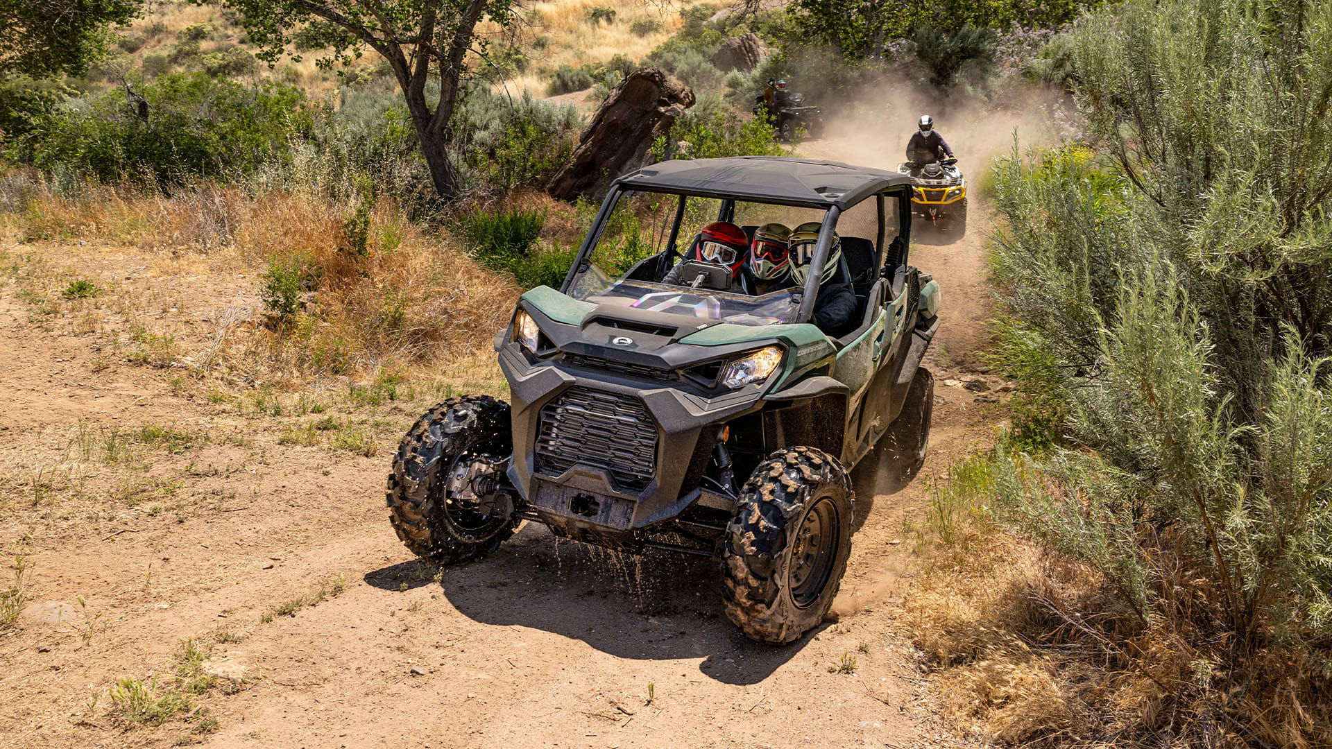 Three riders in a Can-Am Commander going up a dirt trail in the desert