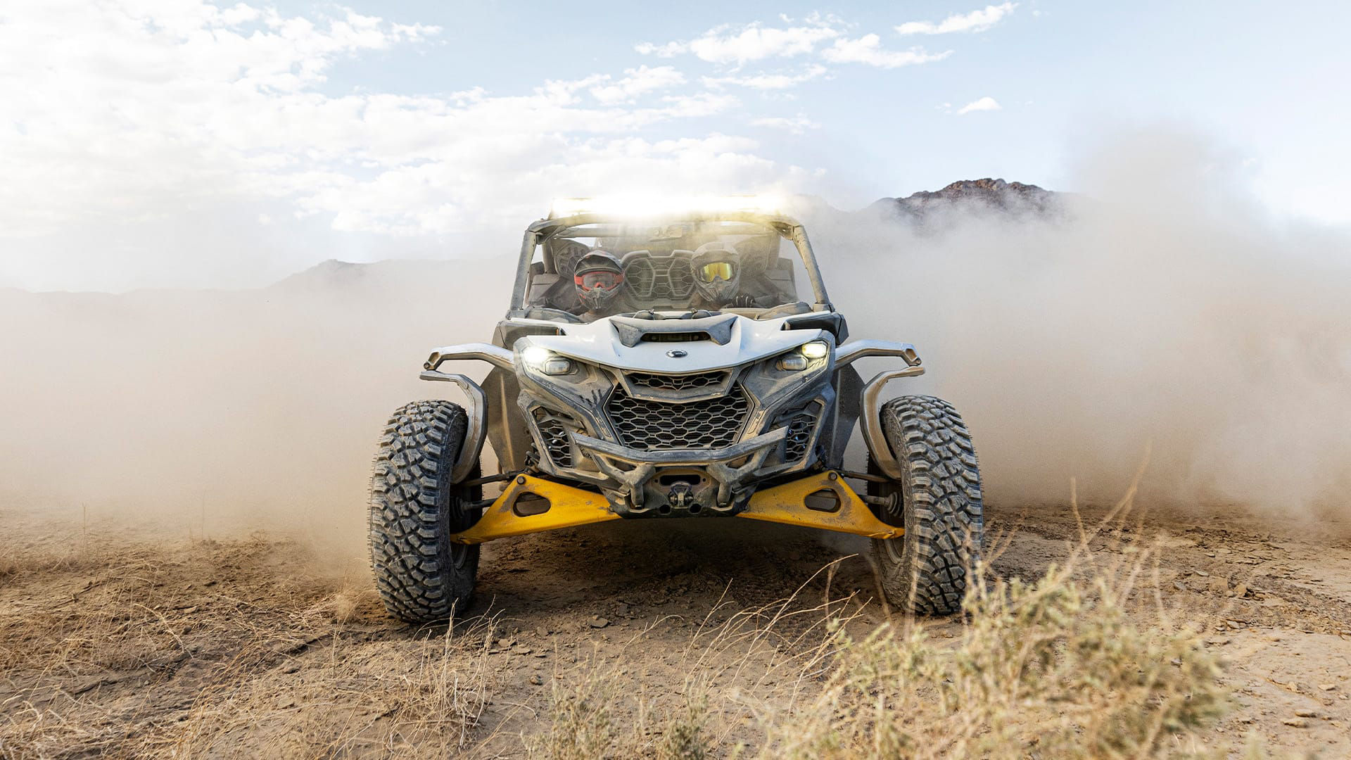 Can-Am Maverick R parked in the desert with dust clouds in the background