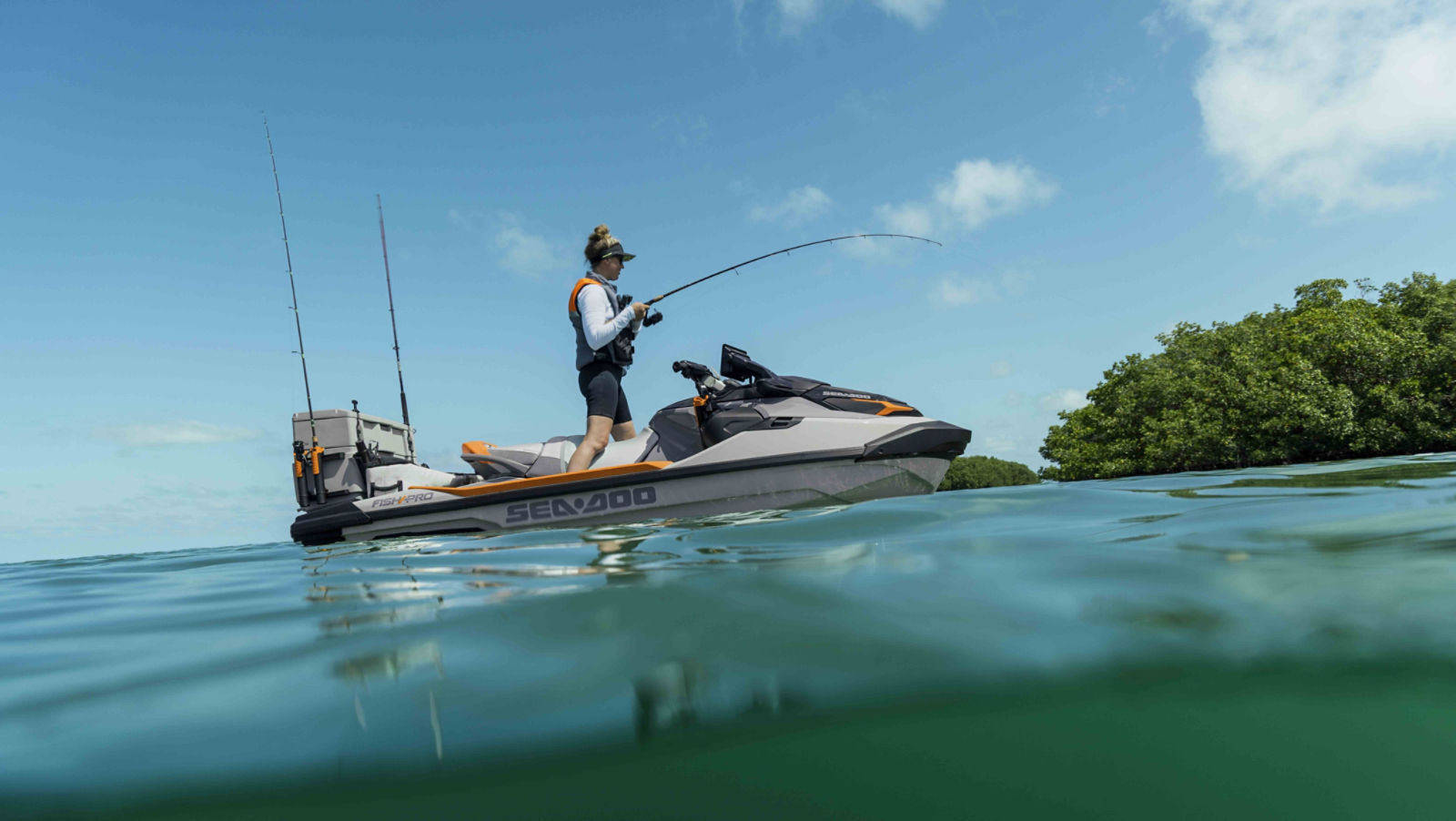 A man wearing polarized sunglasses in the water with two Sea-Doo personal watercraft behind him, with a woman sitting on one of it