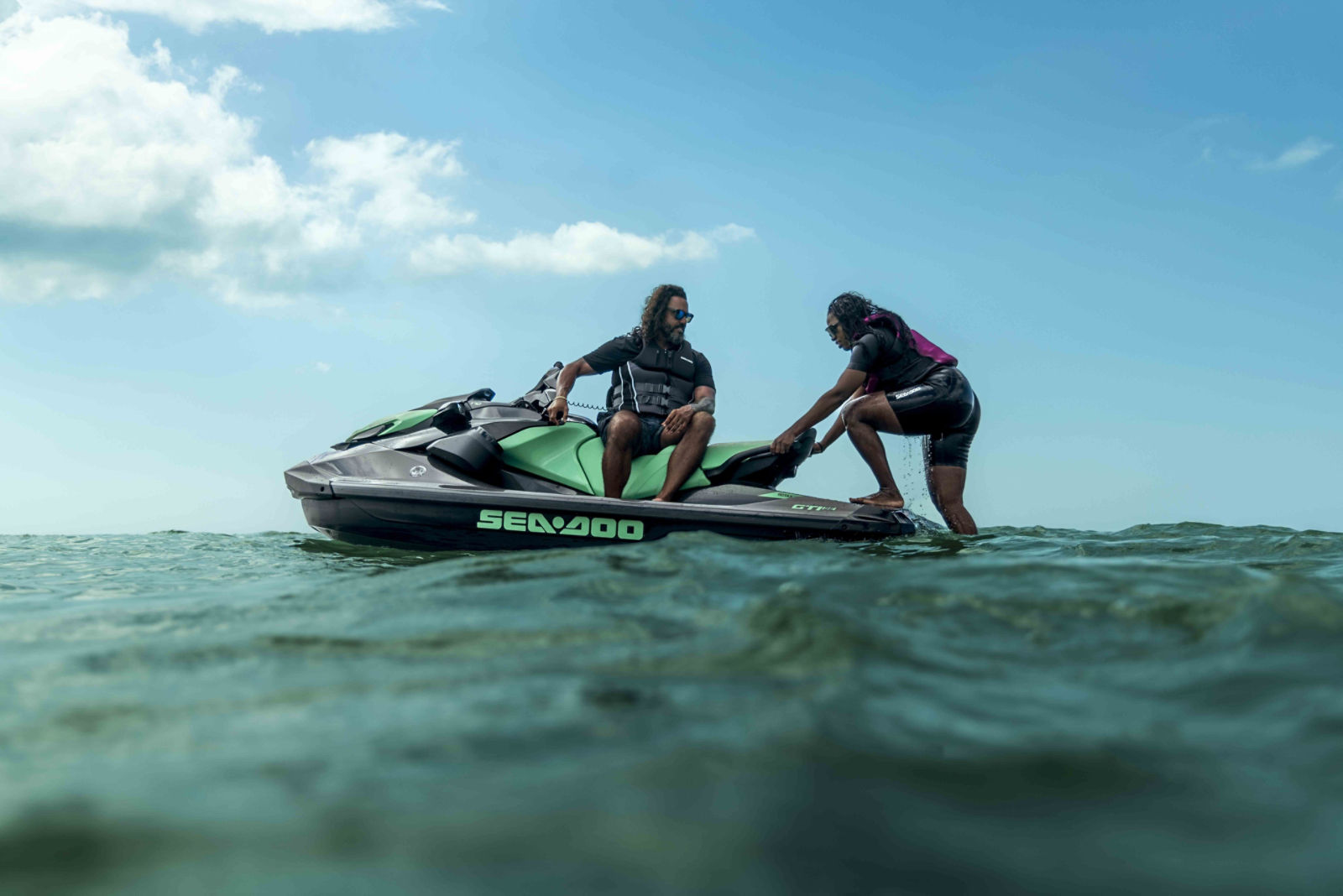 Deux personnes à bord d’un Sea-Doo GTI SE dans des eaux peu profondes, dont l’une est en train de monter à bord
