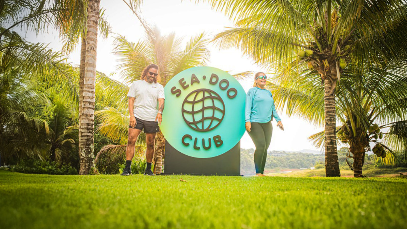 Two people next to the Sea-Doo social club logo near palm trees