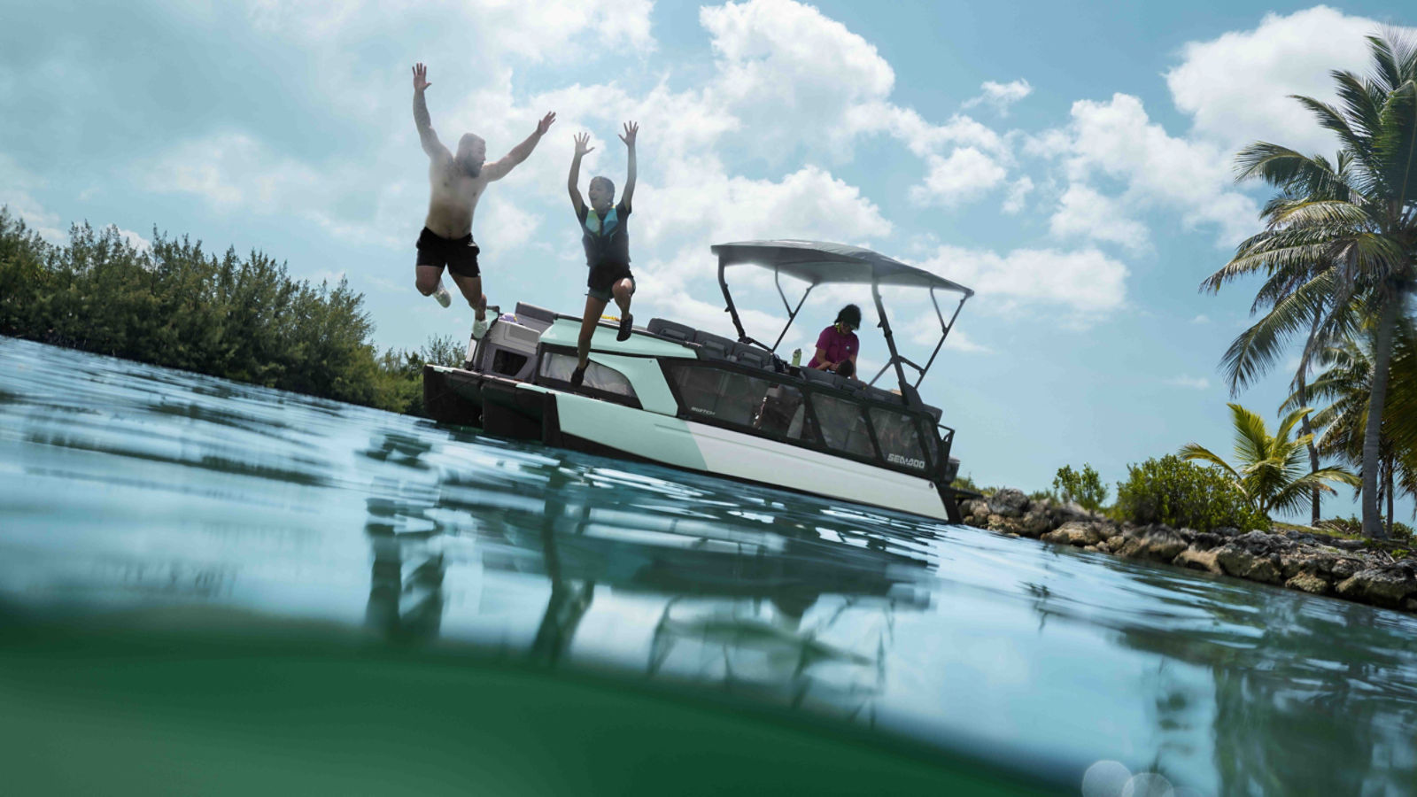 A family jumping into the water near their 2026 Sea-Doo Switch Cruise pontoon boat