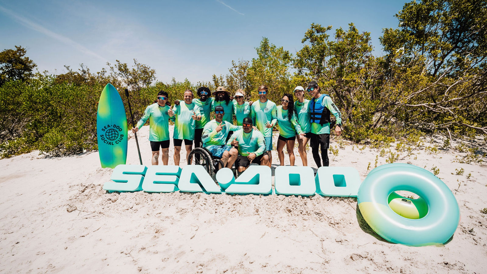 Members of the Sea-Doo Social Club posing together for a photo on the sand.