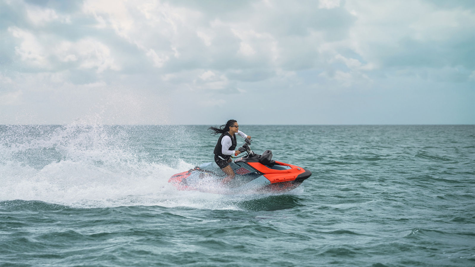 A woman riding a brand-new 2027 Sea-Doo Spark X Trixx personal watercraft on a lake