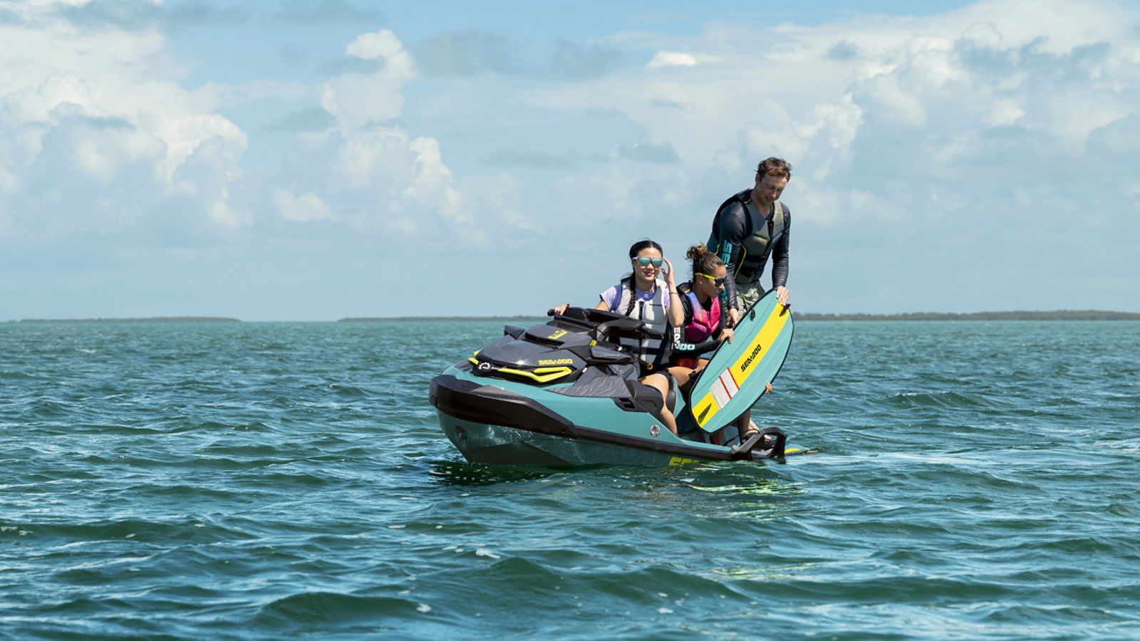 Three riders aboard a new 2027 Sea-Doo Wake Pro PWC holding a Sea-Doo wakeboard on open water