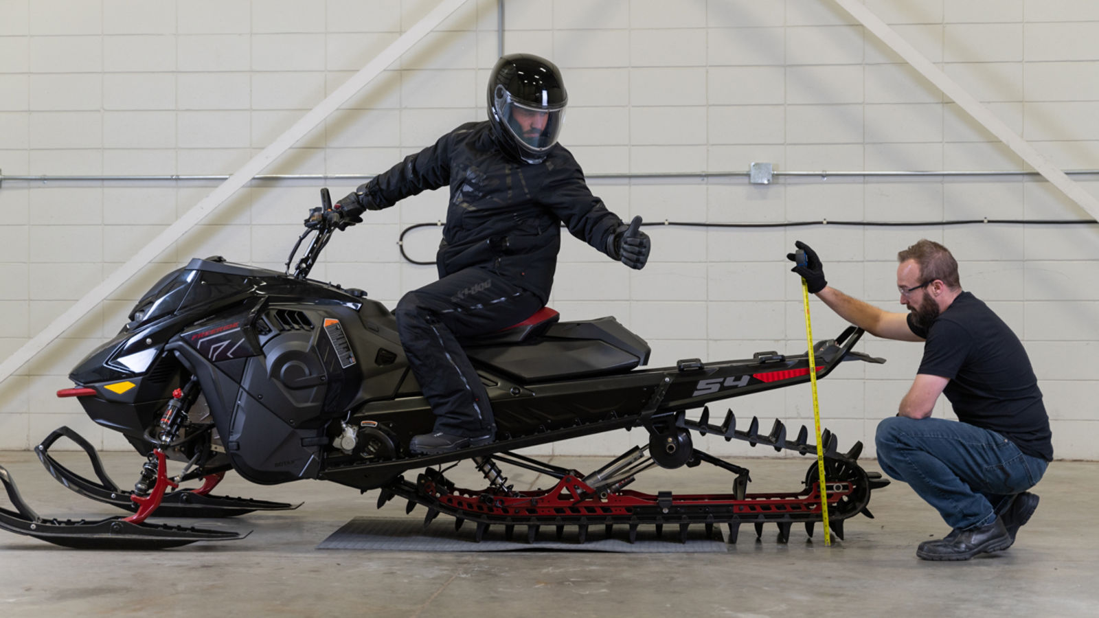 Rider on a Ski-Doo snowmobile while a colleague measures the height of the tracks