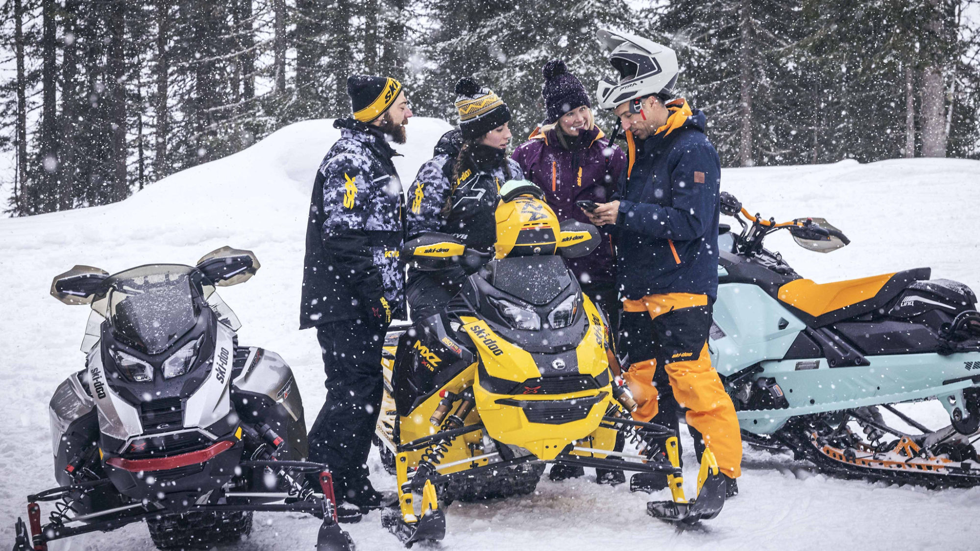Groupe de motoneigistes regardant un cellulaire à côté de leurs Ski-Doo