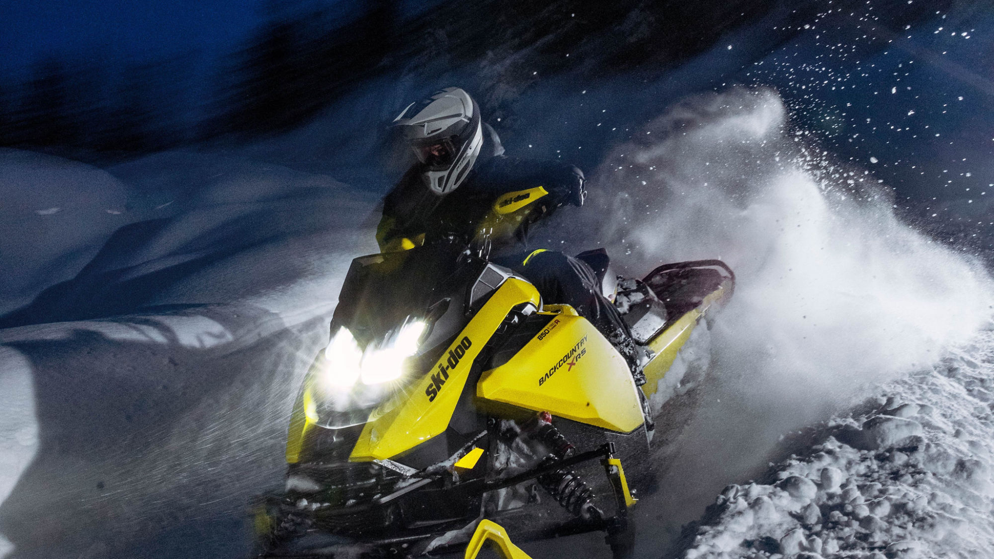 Un motoneige muti-segment 2025 de Ski-Doo à pleine vitesse dans une forêt enneigée