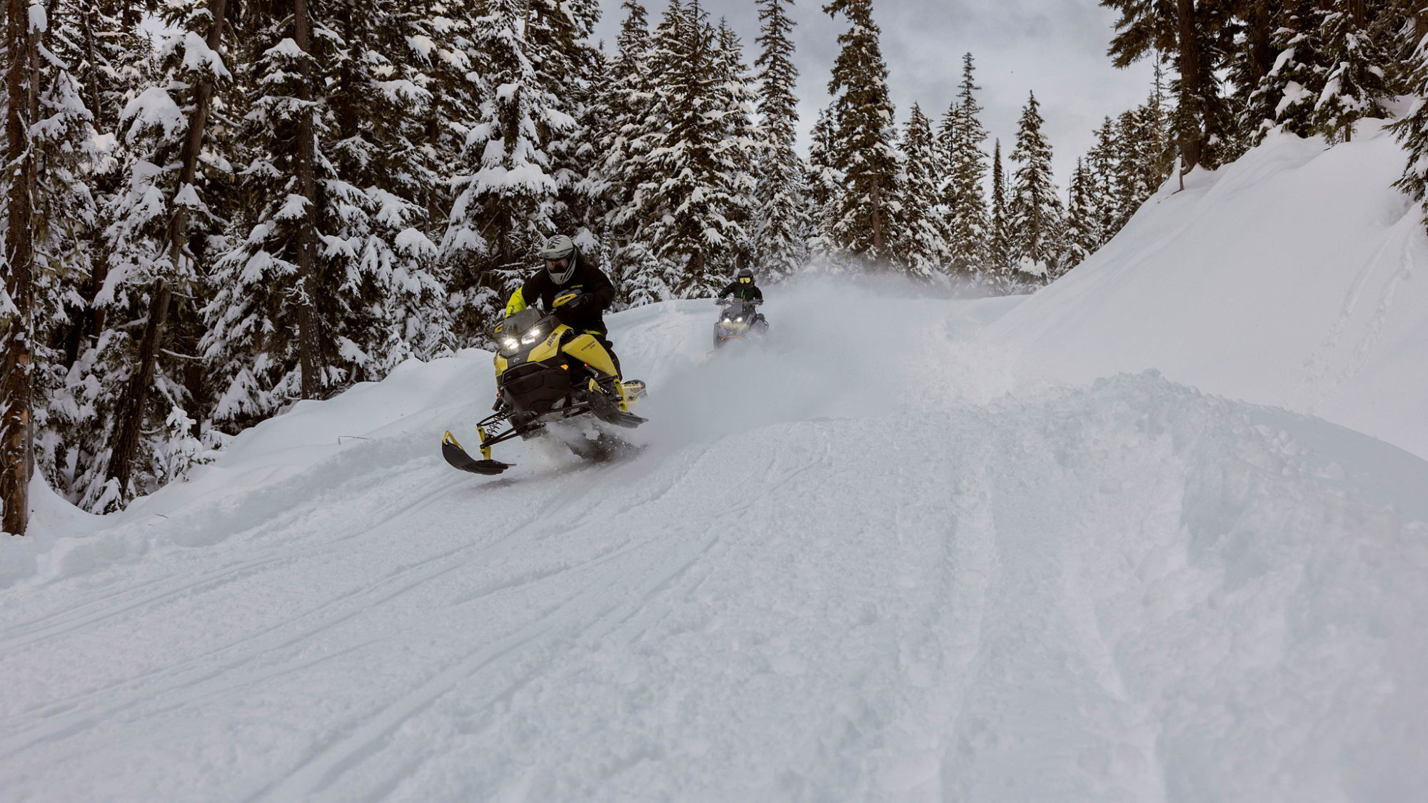 Two 2025 Ski-Doo Crossover snowmobiles riding at high speed in a snowy forest