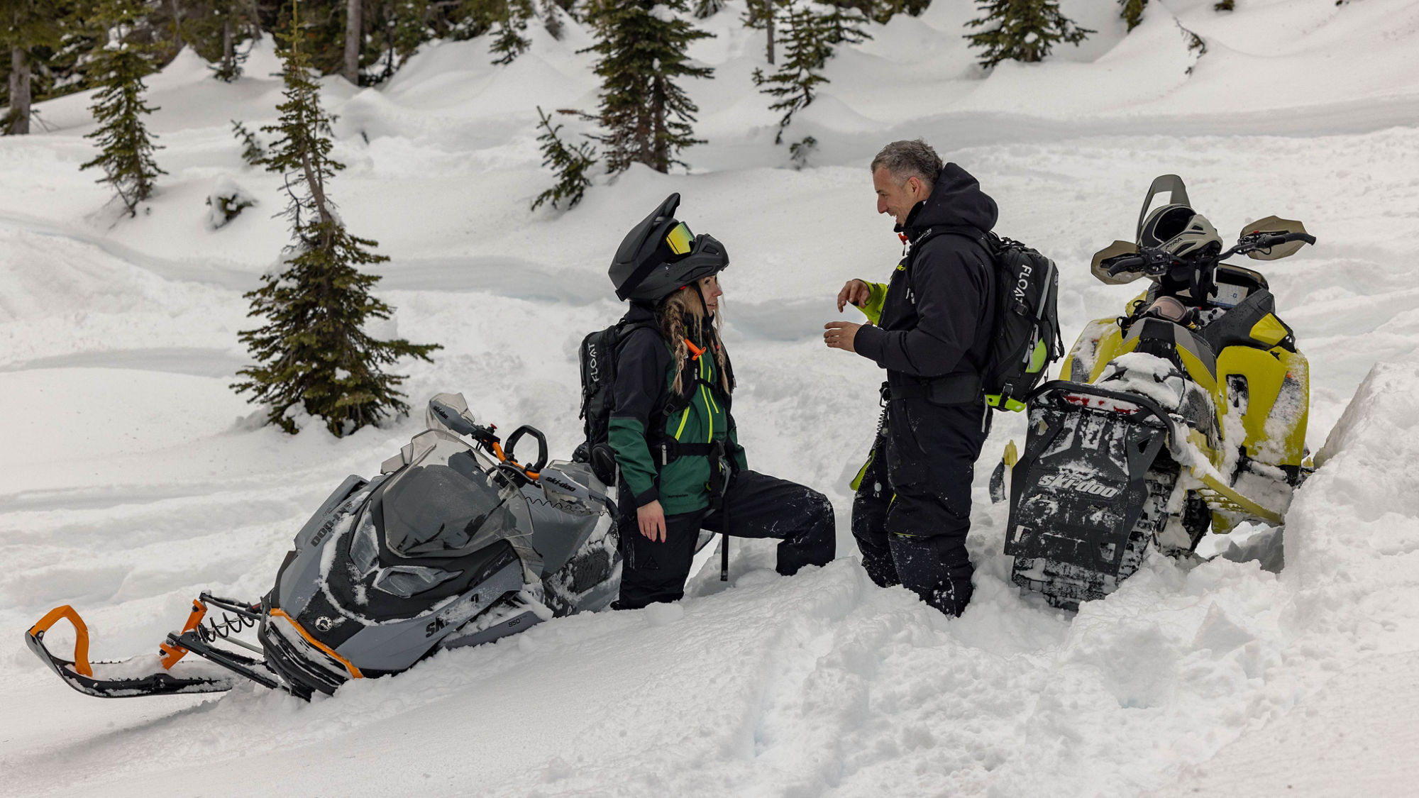 Two riders talking in deep snow next to their Ski-Doo snowmobiles
