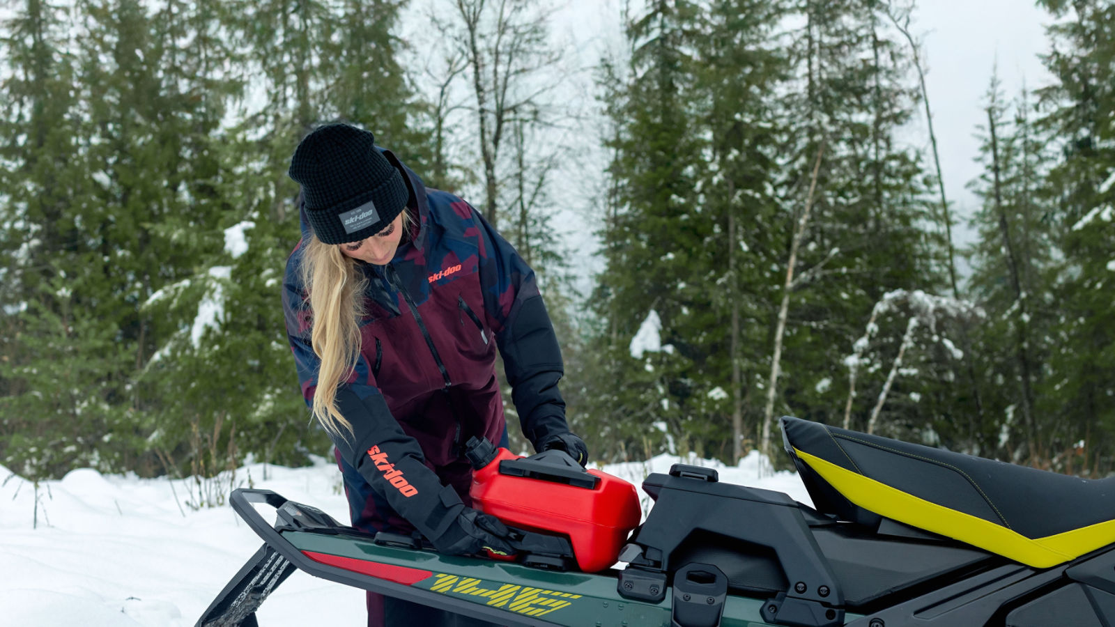 A woman installing a LinQ fuel canister to the back of a snowmobile.